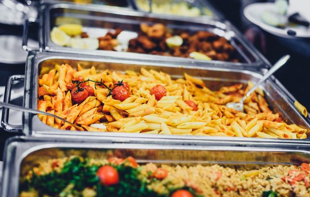A close-up view of a catering buffet warm server tray filled with cooked chicken breasts and cherry tomatoes.